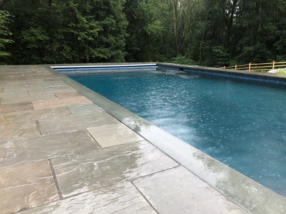 Réalisation d'un piscine avec aménagement paysager arrière design rectangle avec des pavés en pierre naturelle.