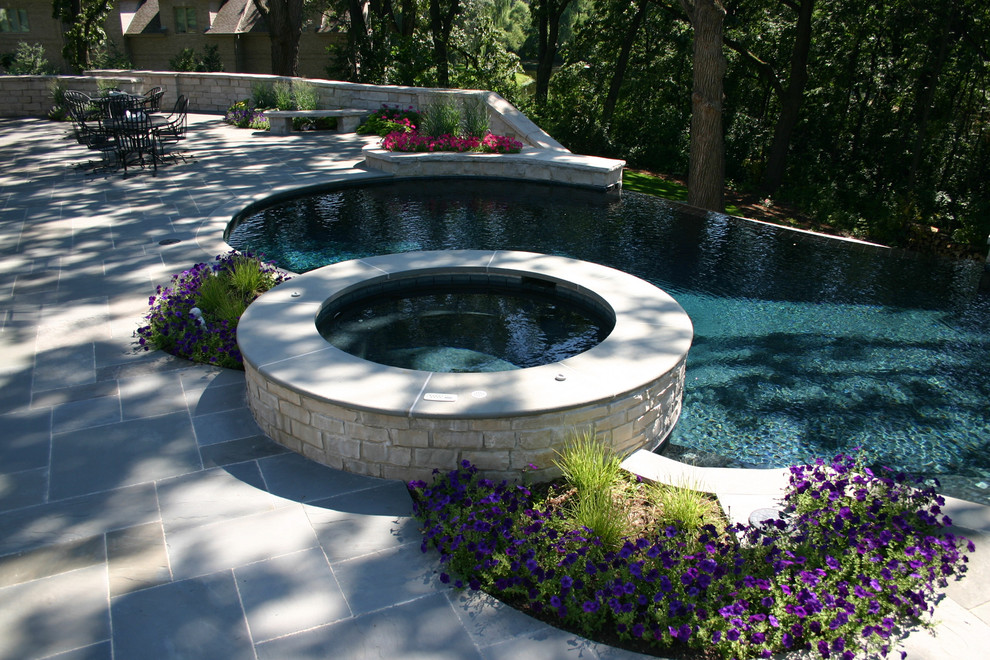 Esempio di una grande piscina a sfioro infinito classica a "C" in cortile con fontane e pavimentazioni in pietra naturale