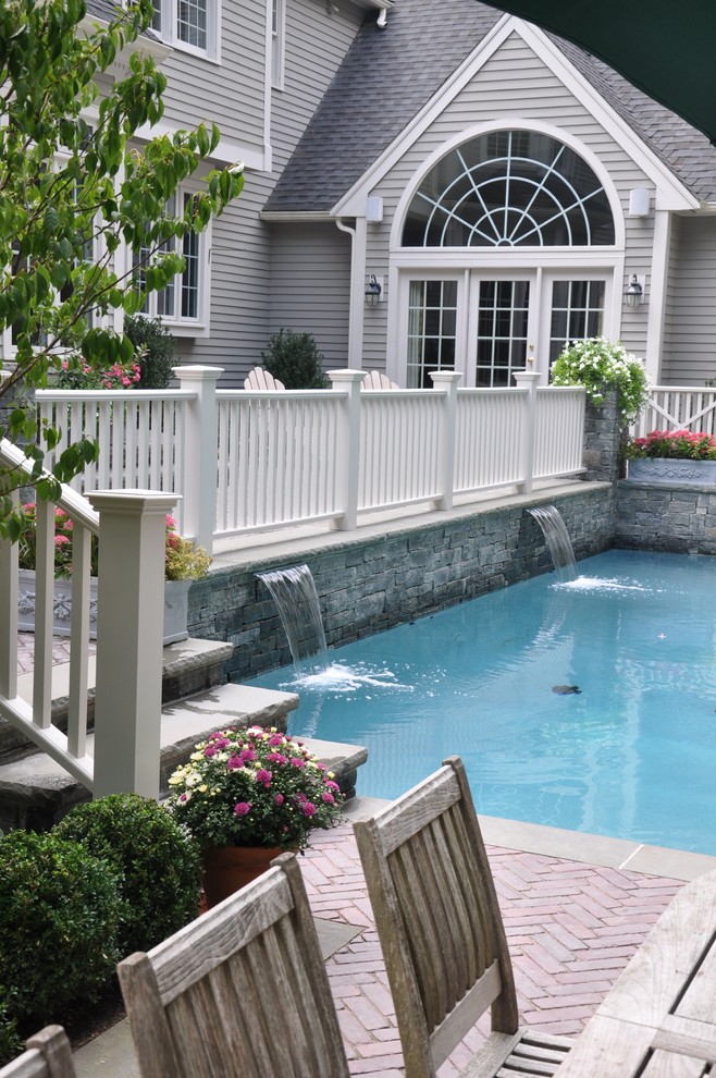 Modelo de piscinas y jacuzzis alargados clásicos de tamaño medio rectangulares en patio trasero con adoquines de ladrillo