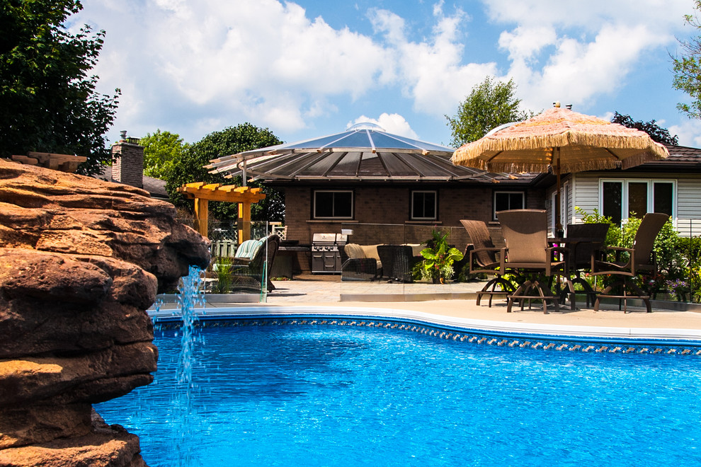 Foto di una grande piscina monocorsia tropicale a "C" dietro casa con fontane e piastrelle