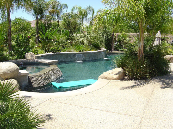 Ispirazione per una piscina naturale tropicale personalizzata di medie dimensioni e dietro casa con lastre di cemento e una vasca idromassaggio