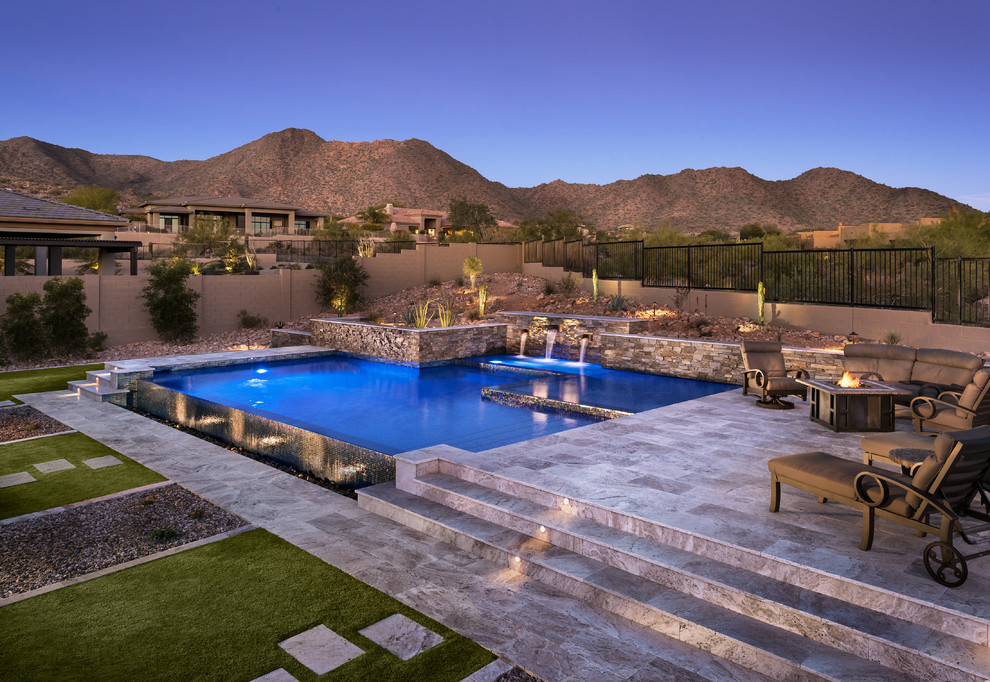Medium sized back custom shaped infinity swimming pool in Phoenix with a water feature and natural stone paving.