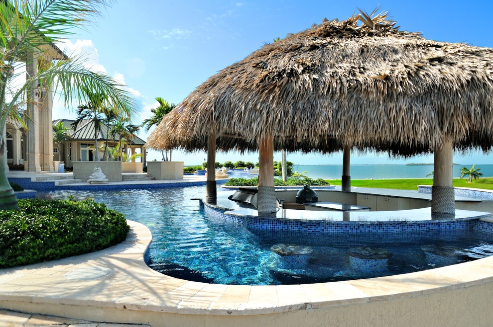 Ejemplo de piscina con fuente infinita tropical extra grande a medida en patio trasero con suelo de baldosas