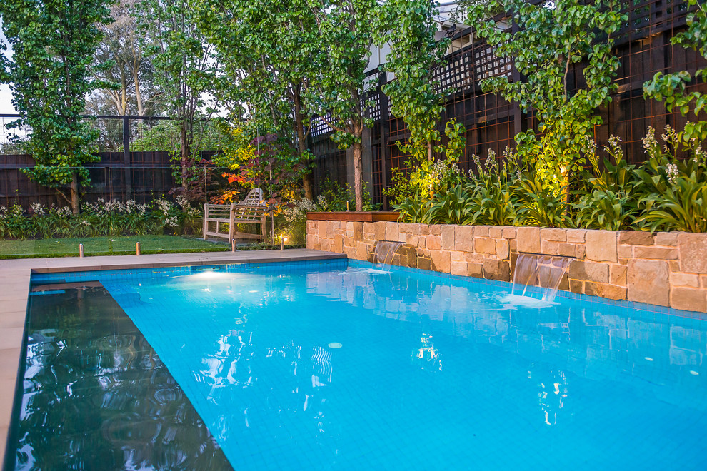 Ejemplo de piscina con fuente alargada actual pequeña rectangular en patio trasero con adoquines de piedra natural