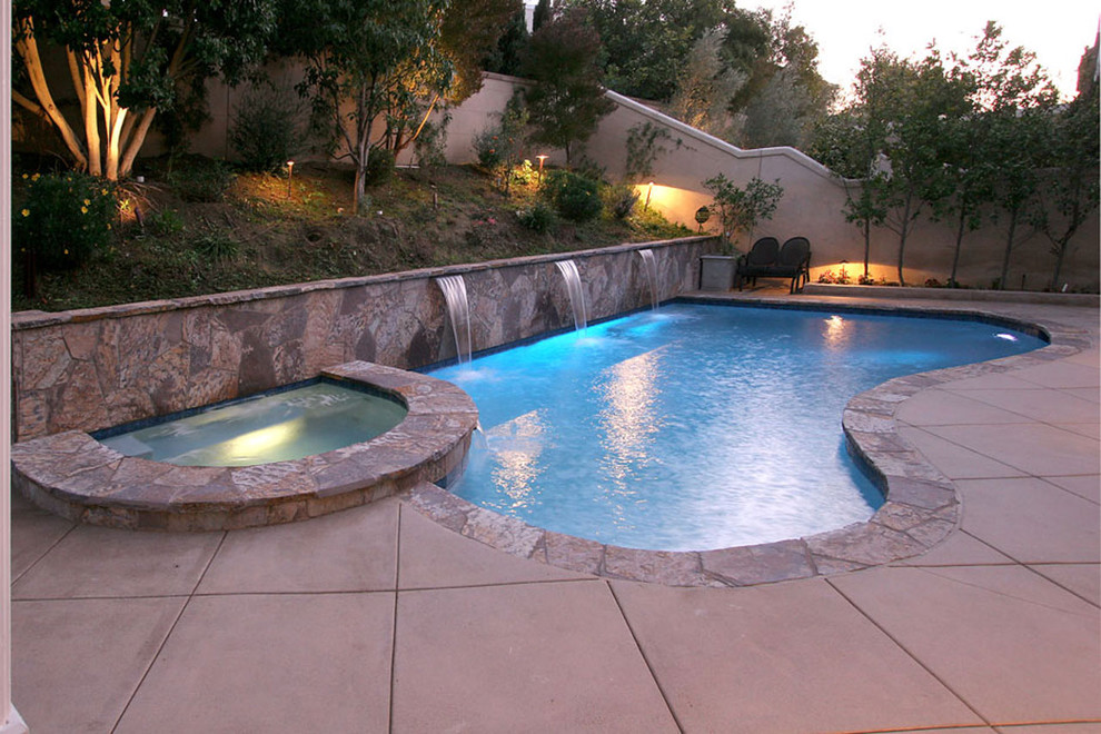 Medium sized traditional back kidney-shaped natural hot tub in Orange County with concrete slabs.