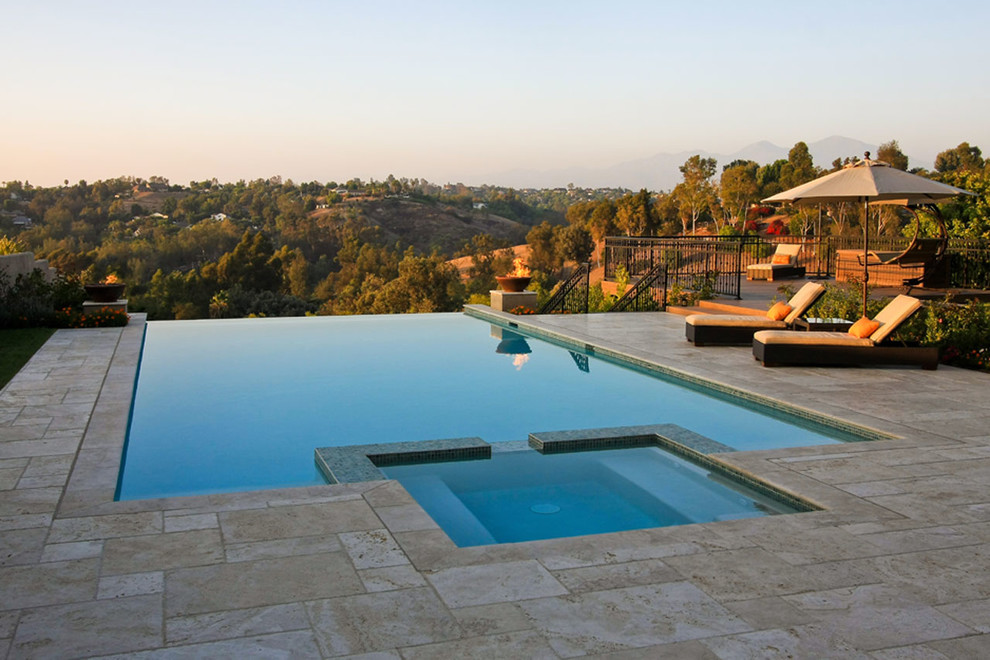 Exemple d'une piscine à débordement et arrière tendance de taille moyenne et rectangle avec un bain bouillonnant et des pavés en pierre naturelle.