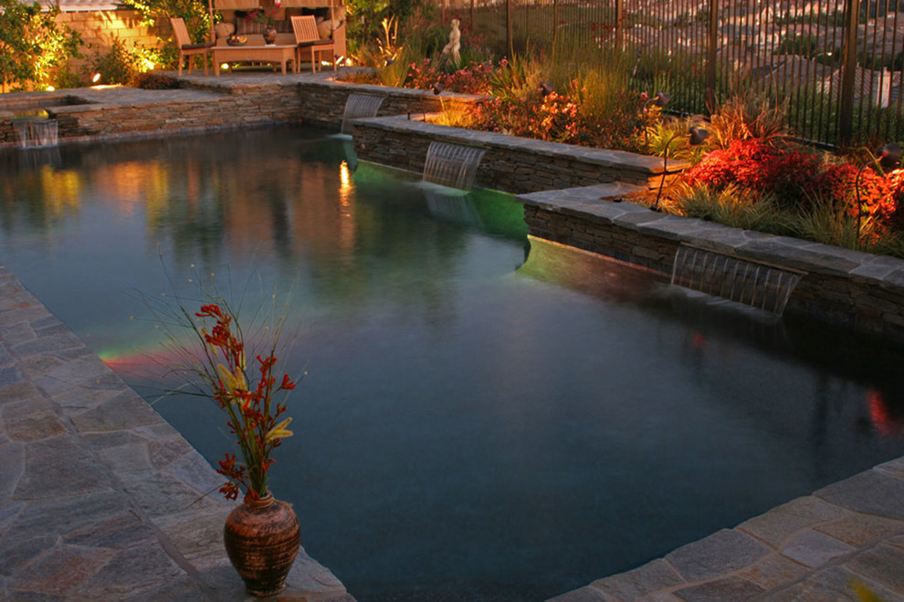 Cette photo montre une grande piscine naturelle et arrière chic en L avec un point d'eau et des pavés en pierre naturelle.