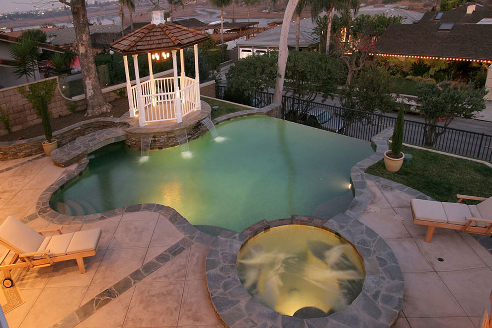 Design ideas for a medium sized classic back custom shaped infinity swimming pool in Orange County with concrete paving.
