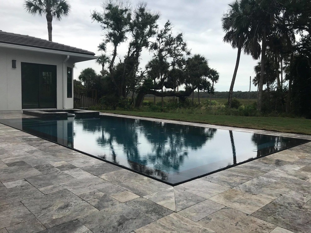 Medium sized modern back rectangular infinity hot tub in Jacksonville with natural stone paving.