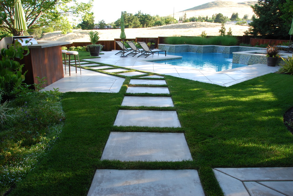 На фото: большой бассейн произвольной формы на заднем дворе в стиле модернизм с джакузи и покрытием из бетонных плит