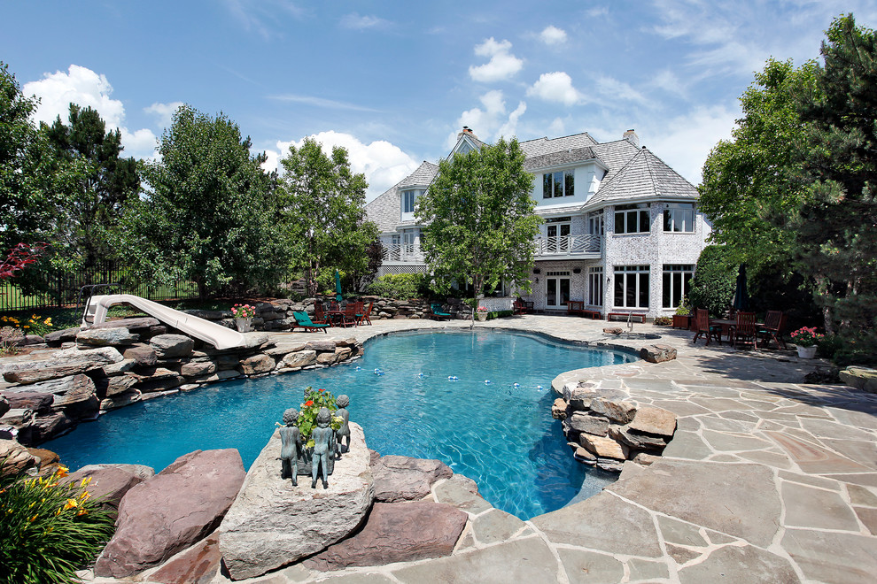 Diseño de piscina con tobogán alargada clásica a medida en patio trasero con adoquines de piedra natural