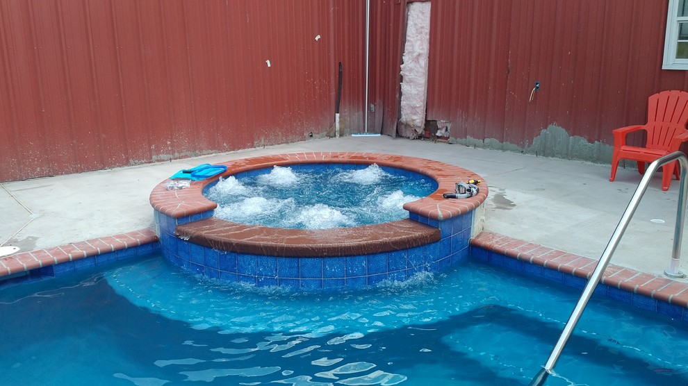 Immagine di una piscina monocorsia country rettangolare di medie dimensioni e dietro casa con una vasca idromassaggio e lastre di cemento
