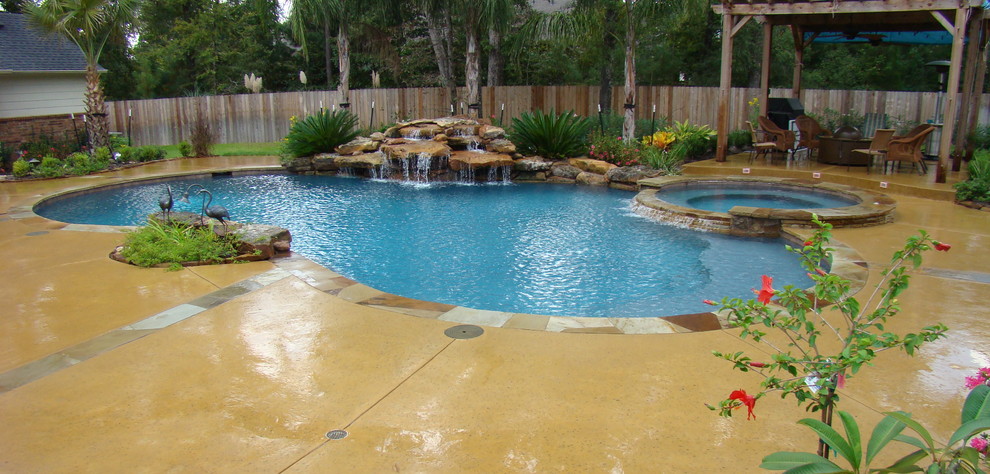 Large elegant backyard stamped concrete and custom-shaped hot tub photo in Houston