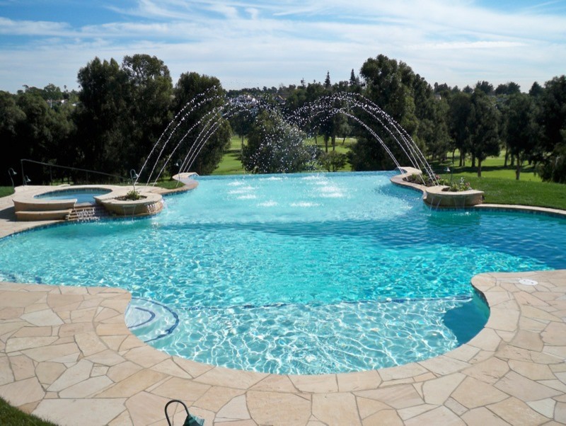 Aménagement d'une piscine arrière et à débordement classique de taille moyenne et sur mesure avec un bain bouillonnant et des pavés en pierre naturelle.