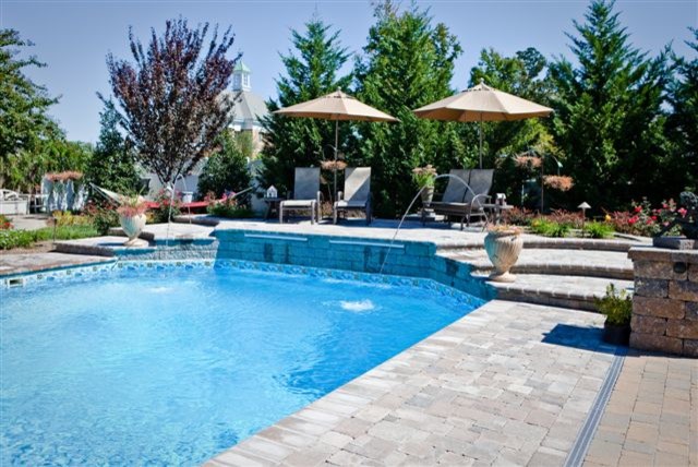 На фото: большой прямоугольный бассейн на заднем дворе в классическом стиле с фонтаном и мощением клинкерной брусчаткой