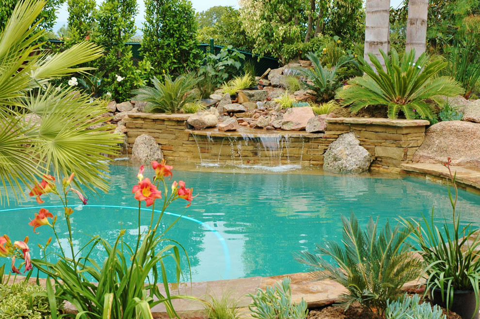 Imagen de piscina con fuente natural tropical pequeña a medida en patio trasero con adoquines de piedra natural