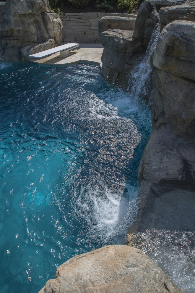 Cette image montre une très grande piscine arrière et naturelle sur mesure avec un point d'eau et des pavés en pierre naturelle.