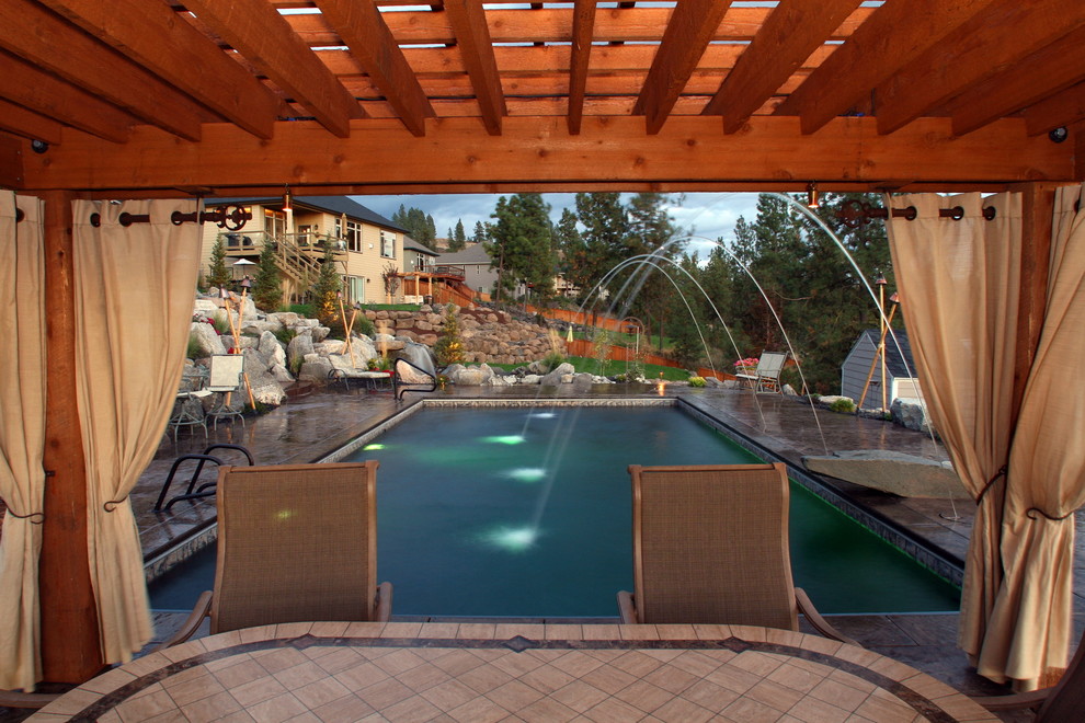 Ejemplo de piscina con fuente tradicional grande rectangular en patio trasero con adoquines de piedra natural