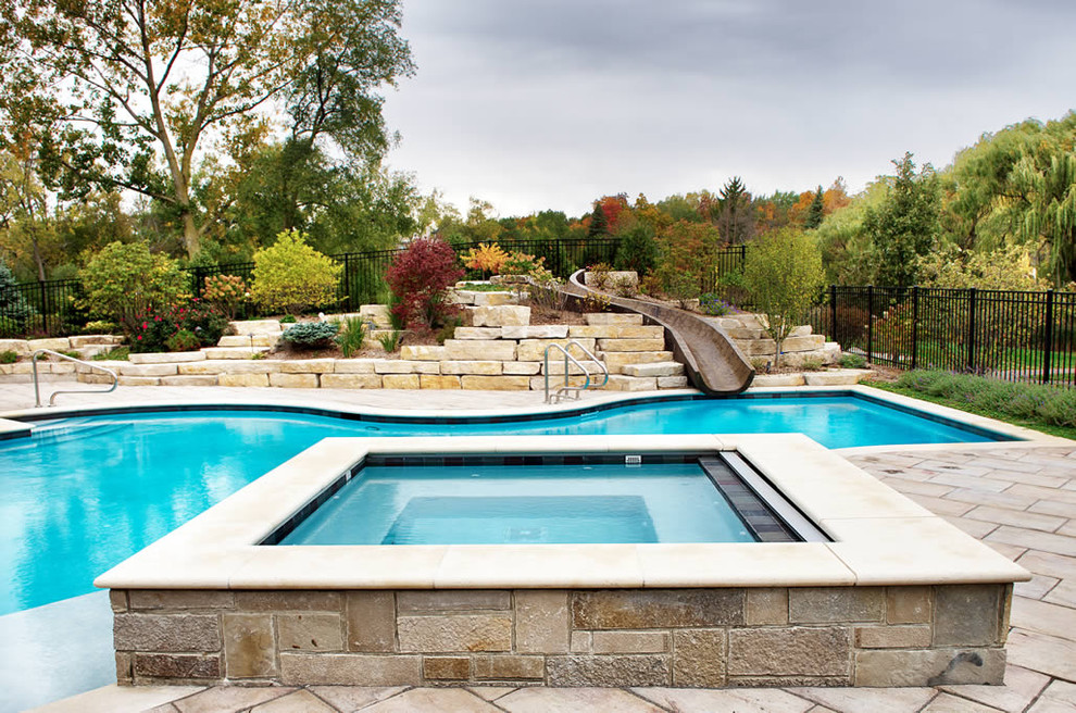 Diseño de piscina con tobogán alargada clásica grande a medida en patio trasero con suelo de baldosas