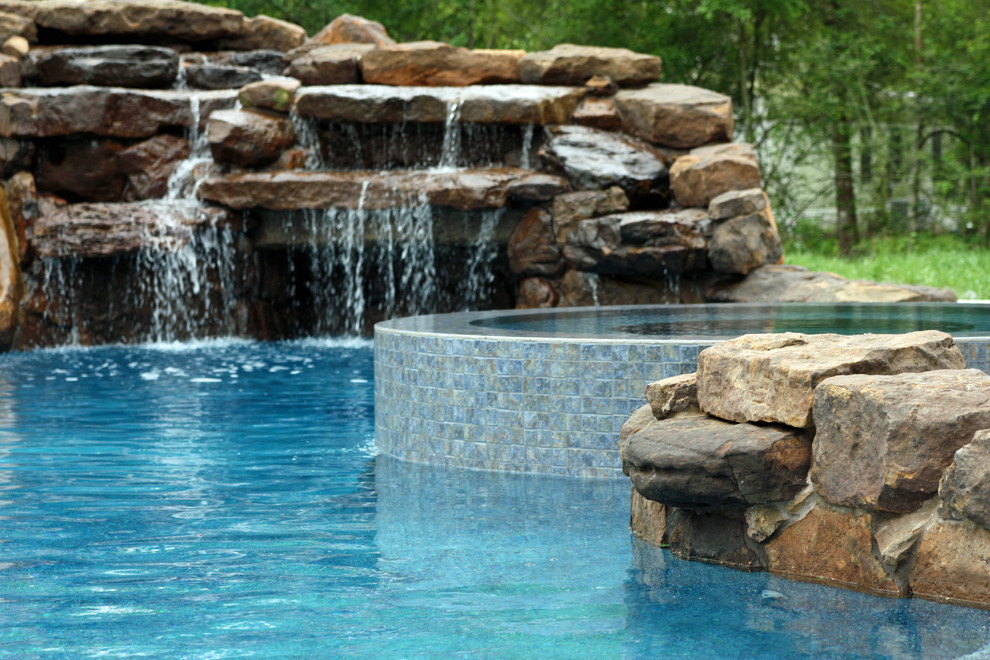 На фото: большой естественный бассейн произвольной формы на заднем дворе в классическом стиле с водной горкой и покрытием из каменной брусчатки с