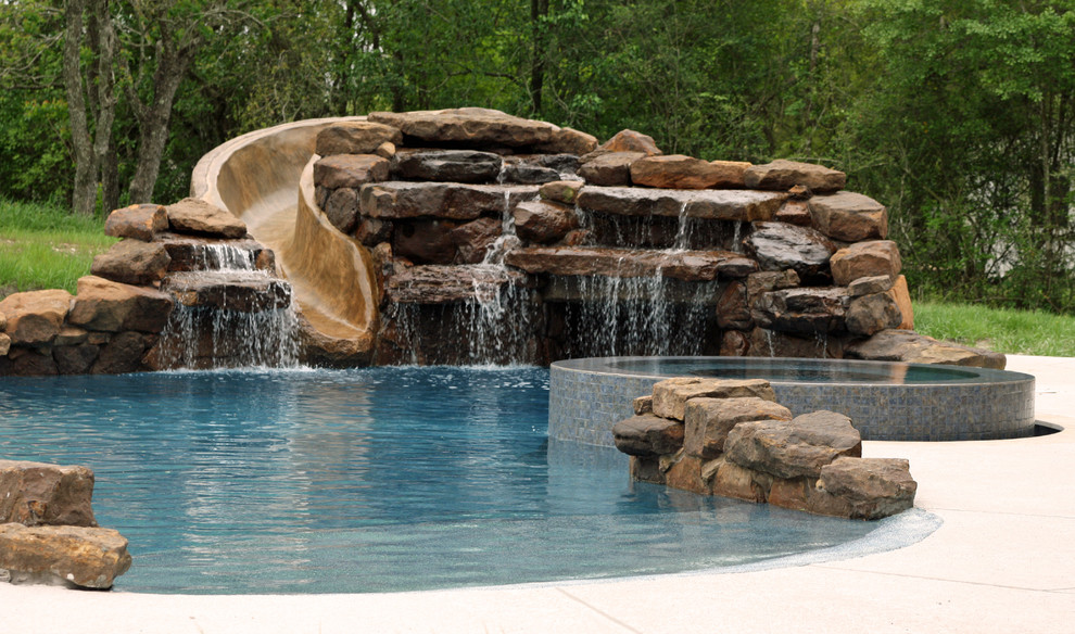 Imagen de piscina con tobogán clásica grande a medida en patio trasero con adoquines de piedra natural