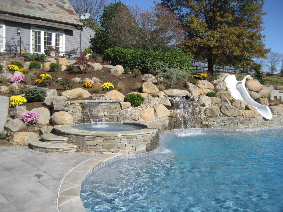 Imagen de piscina con tobogán natural actual grande a medida en patio trasero con adoquines de hormigón