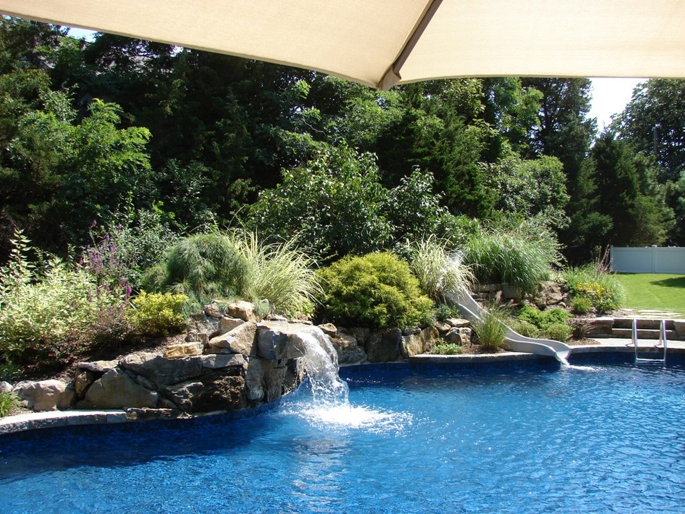 Imagen de piscina con tobogán tradicional grande a medida en patio trasero con adoquines de hormigón