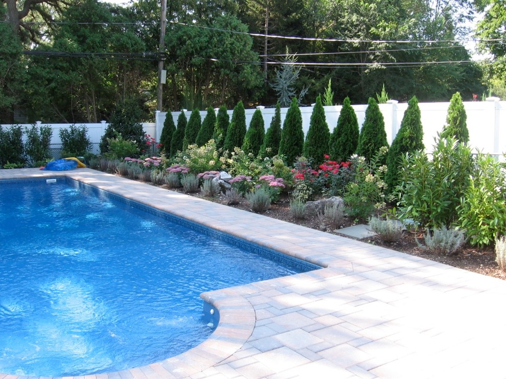 Modelo de piscina natural clásica de tamaño medio rectangular en patio trasero con adoquines de hormigón
