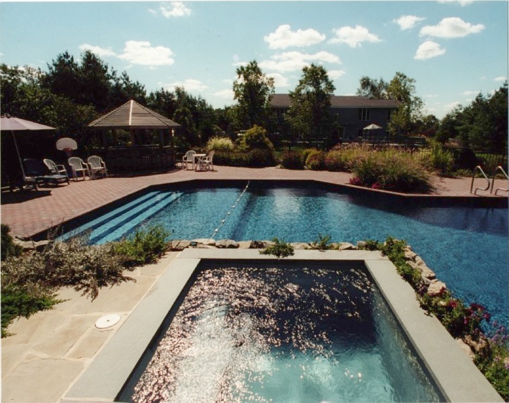 Immagine di una piscina naturale classica personalizzata dietro casa con una vasca idromassaggio e pavimentazioni in pietra naturale