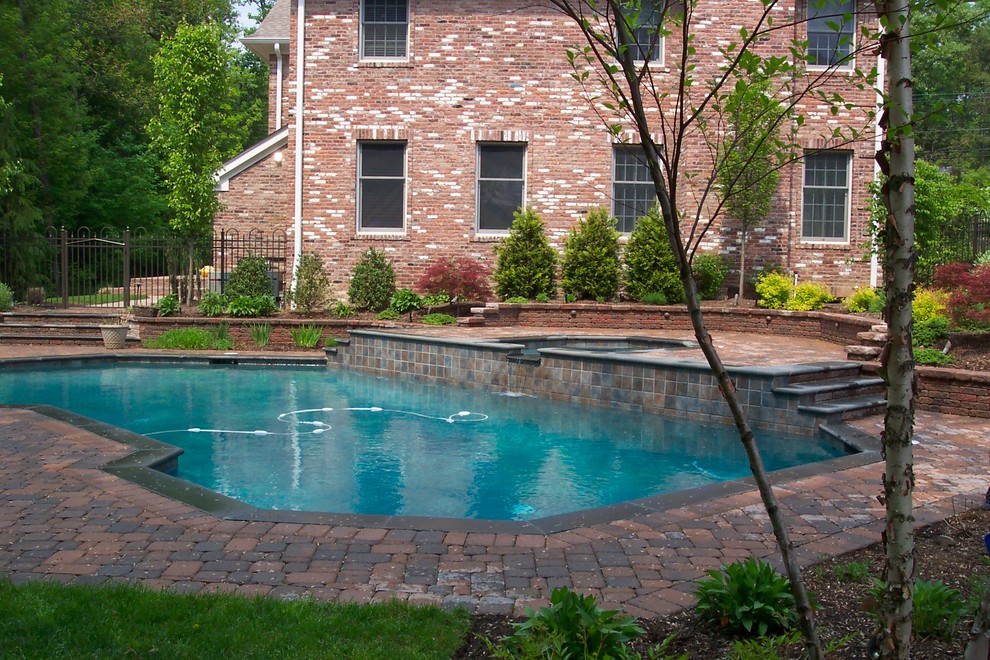Aménagement d'une grande piscine hors-sol et latérale classique sur mesure avec un bain bouillonnant et des pavés en béton.