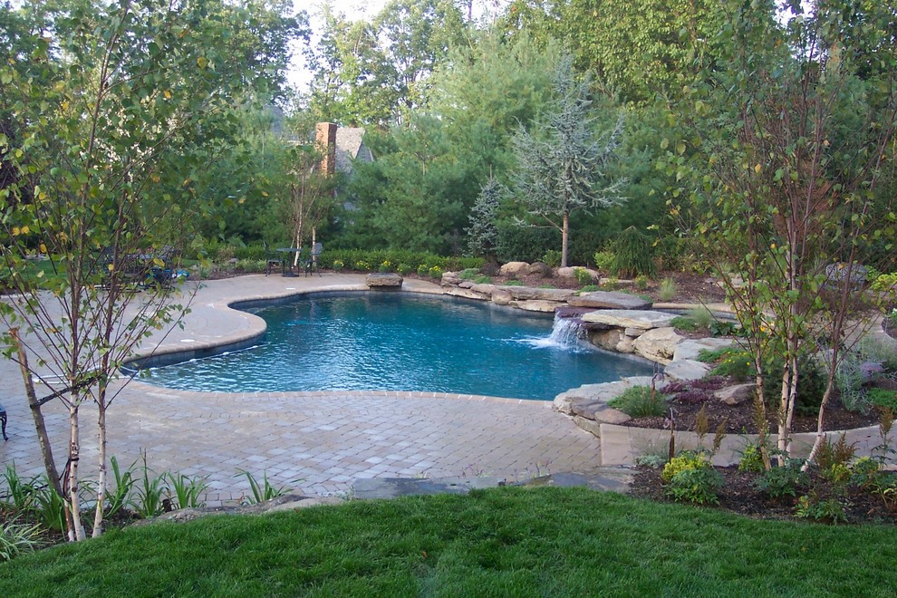 Aménagement d'une grande piscine naturelle et arrière montagne sur mesure avec un bain bouillonnant et des pavés en béton.