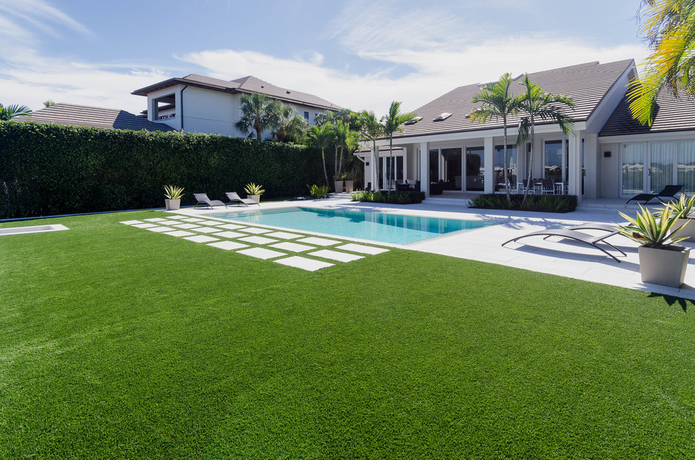 Large island style backyard concrete paver and rectangular lap pool photo in Miami