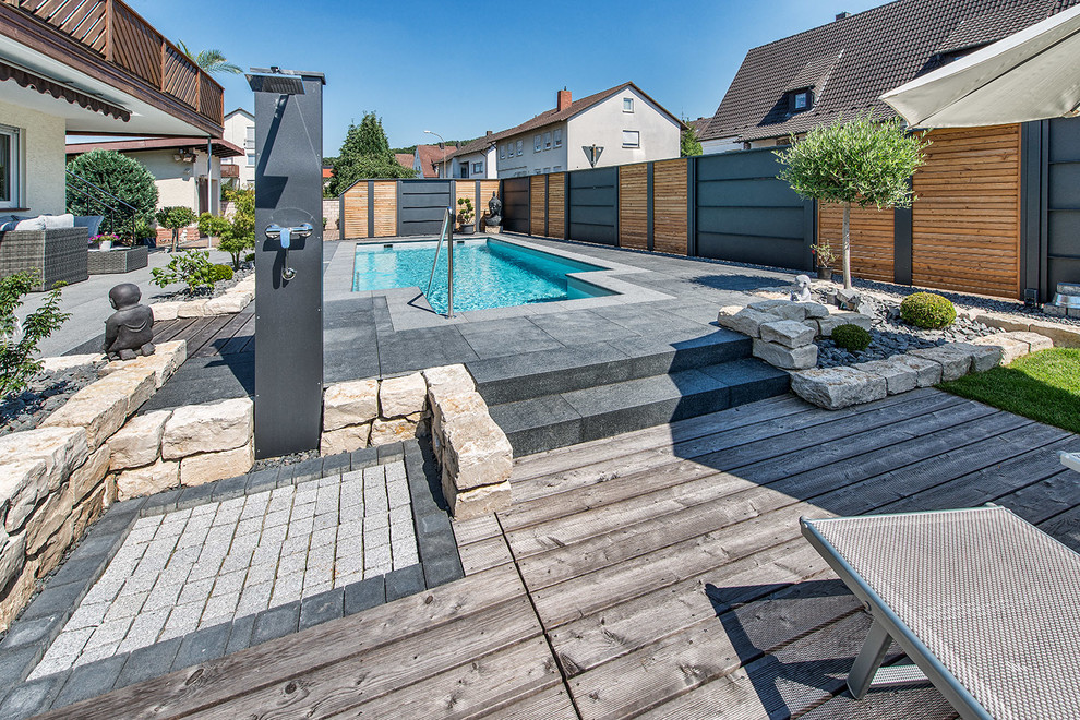 Diseño de piscina alargada actual de tamaño medio a medida en patio trasero con adoquines de hormigón
