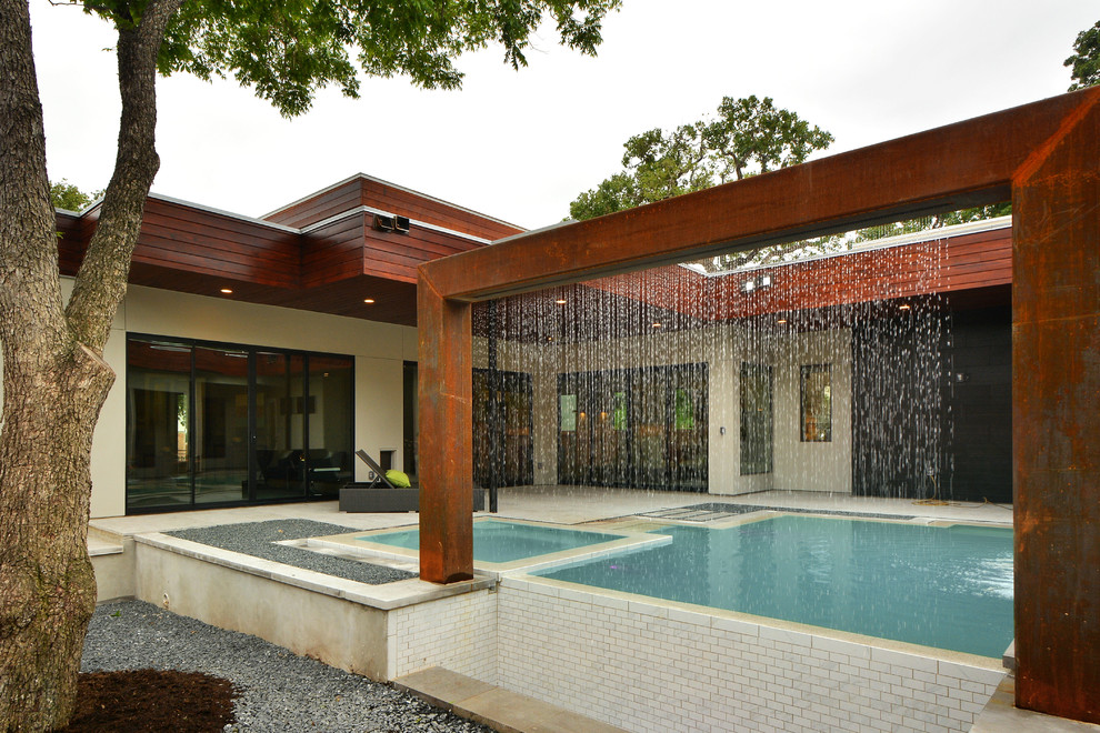 Réalisation d'une grande piscine à débordement et arrière minimaliste sur mesure avec un point d'eau et des pavés en pierre naturelle.