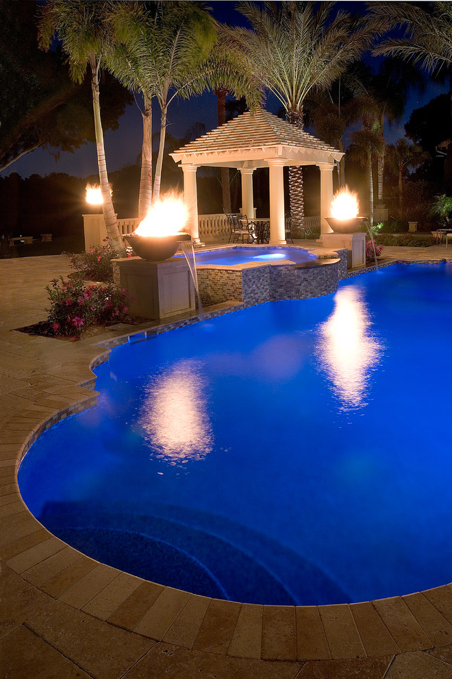 This is an example of a large world-inspired back custom shaped swimming pool in Tampa with a water feature and natural stone paving.