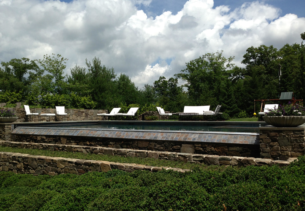 Imagen de piscina con fuente infinita clásica de tamaño medio rectangular en patio trasero con adoquines de piedra natural