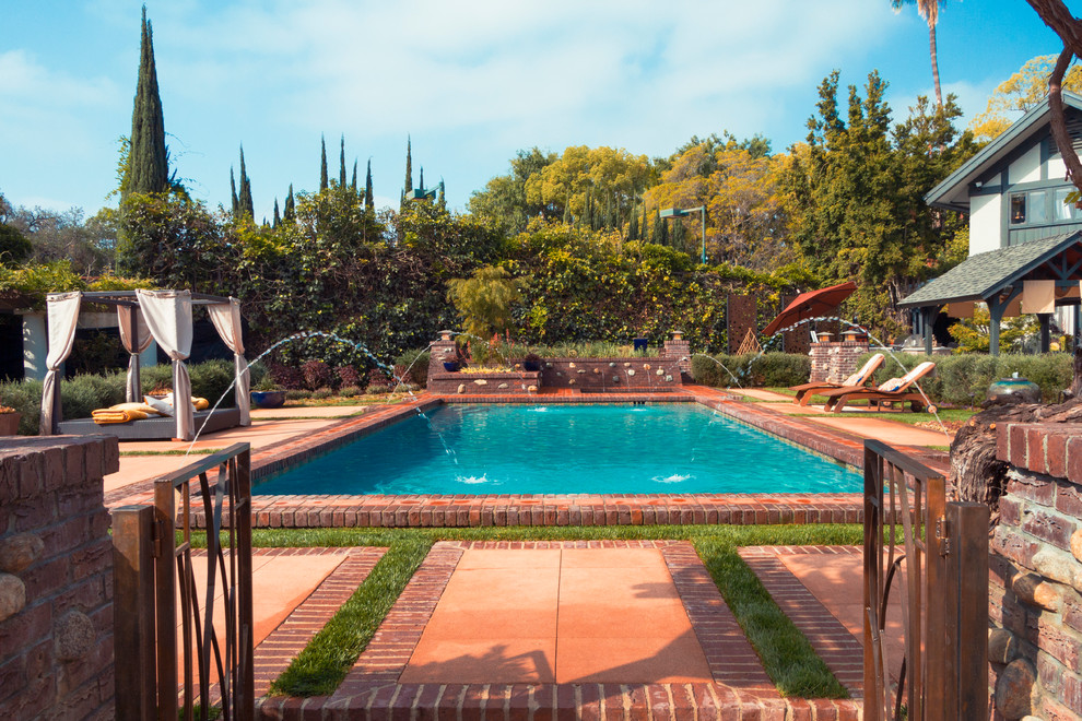 Modelo de piscina con fuente alargada campestre grande rectangular en patio trasero con adoquines de ladrillo
