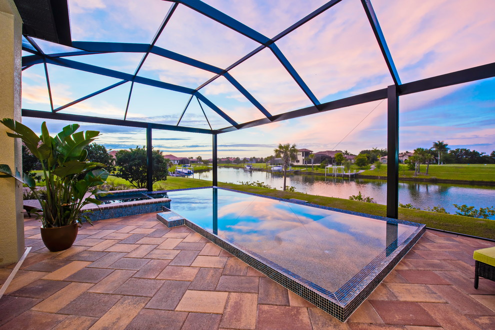 Foto de piscina con fuente infinita campestre grande en forma de L en patio trasero con adoquines de hormigón