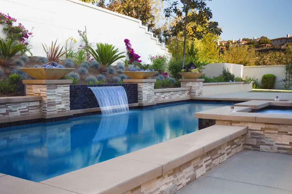 Пример оригинального дизайна: прямоугольный бассейн на заднем дворе в средиземноморском стиле с джакузи и покрытием из бетонных плит