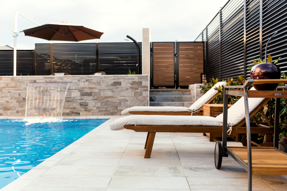 Diseño de piscina con fuente alargada actual de tamaño medio rectangular en patio trasero con suelo de baldosas