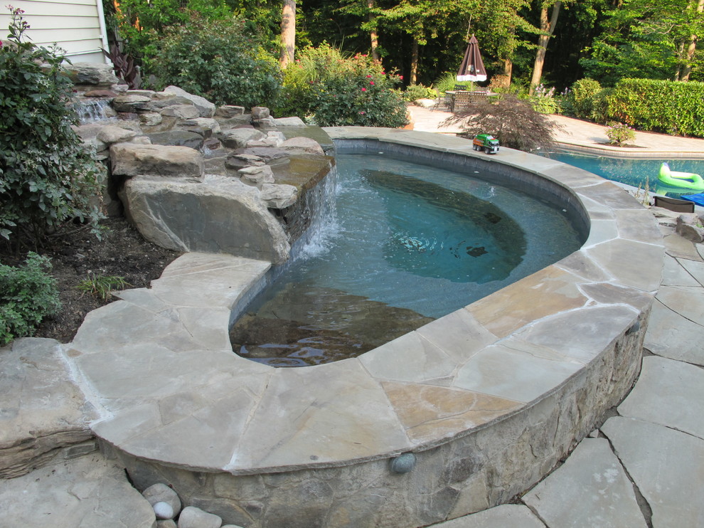 Cette photo montre une piscine naturelle et arrière chic de taille moyenne et sur mesure avec un bain bouillonnant et des pavés en pierre naturelle.