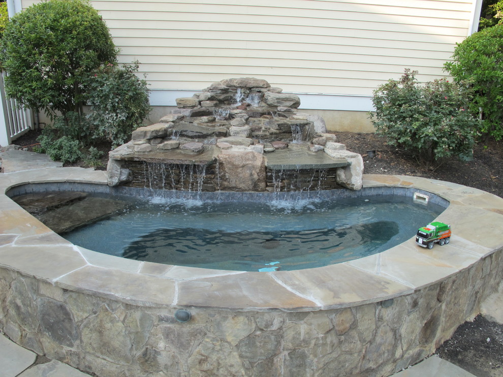 Cette image montre une piscine naturelle et arrière traditionnelle de taille moyenne et sur mesure avec un bain bouillonnant et des pavés en pierre naturelle.