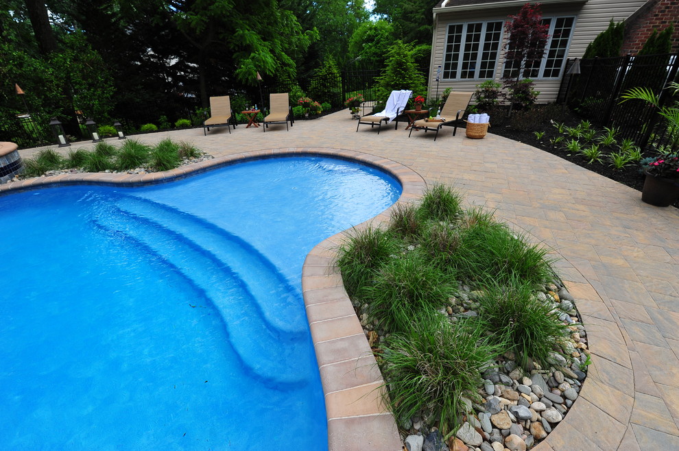 Ejemplo de piscinas y jacuzzis clásicos grandes a medida en patio trasero con adoquines de hormigón