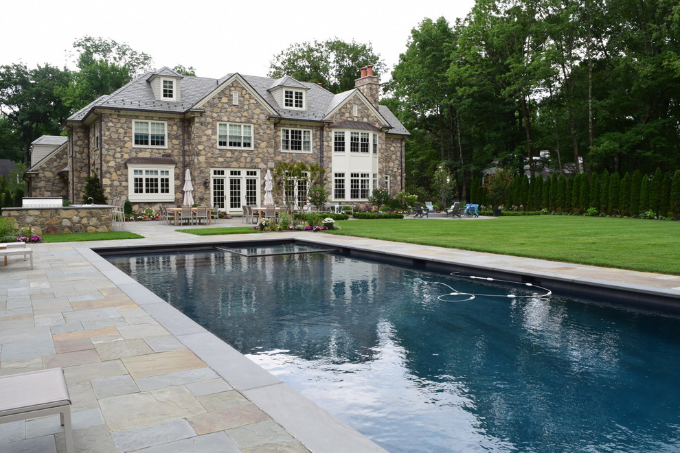 Large traditional back rectangular swimming pool in New York with a pool house and natural stone paving.