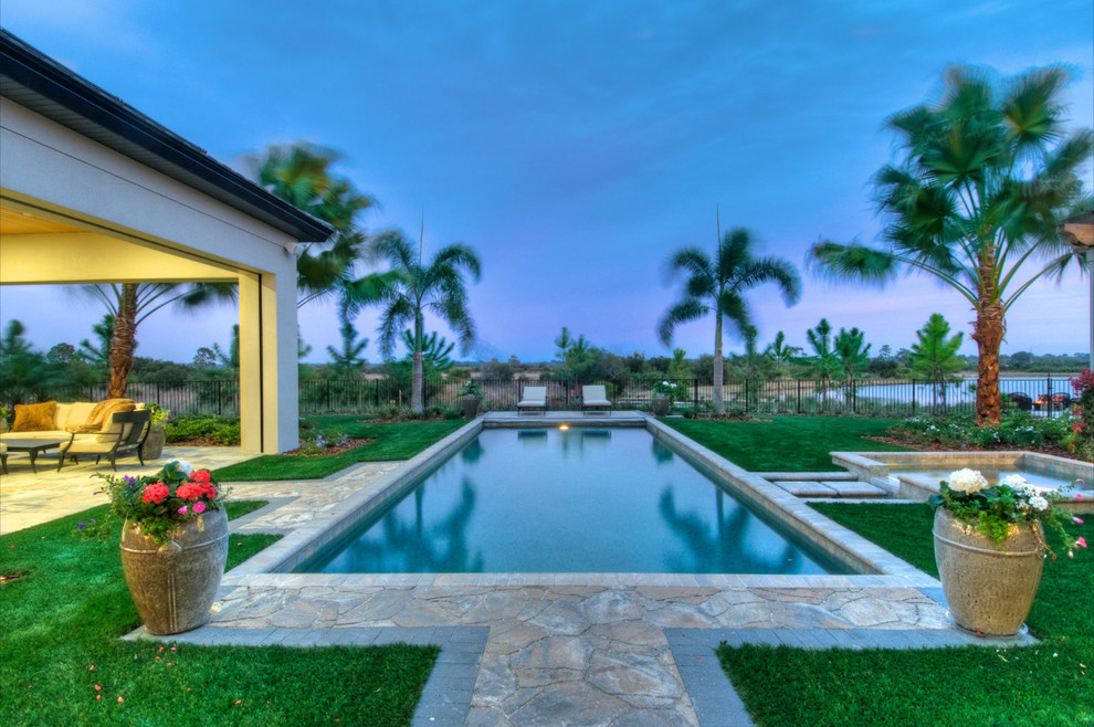 Foto de piscina alargada exótica grande rectangular en patio trasero con adoquines de piedra natural