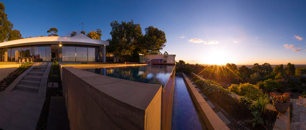 Ejemplo de piscina con fuente infinita de tamaño medio rectangular en patio trasero con adoquines de piedra natural
