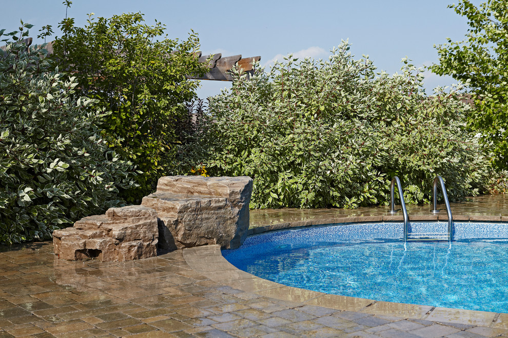 Modelo de piscina con fuente natural actual grande a medida en patio trasero con adoquines de ladrillo