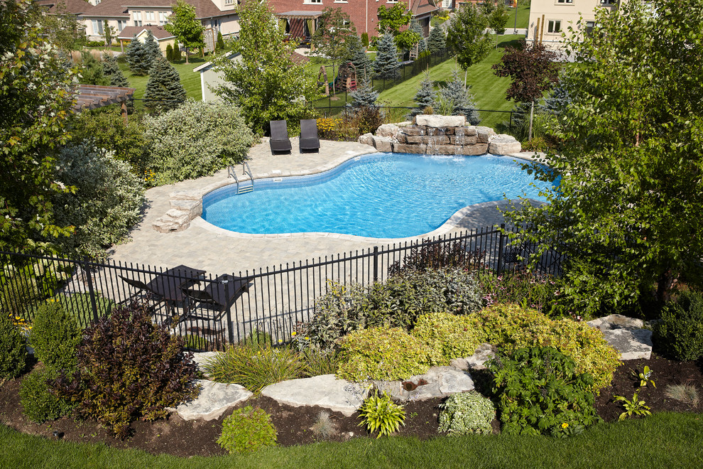 Design ideas for a large contemporary back custom shaped natural swimming pool in Toronto with a water feature and brick paving.