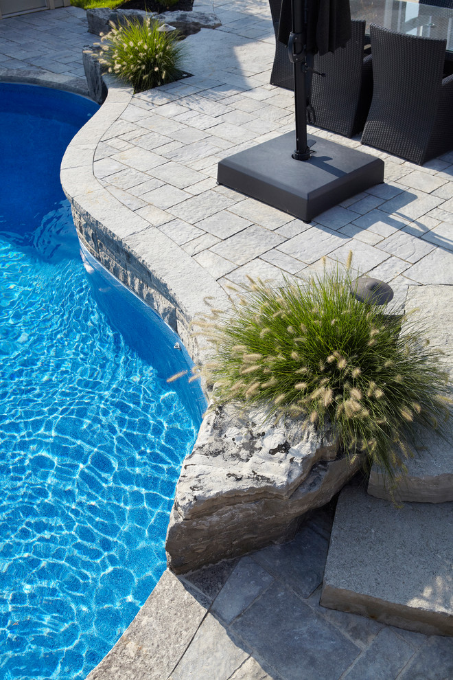 Immagine di una grande piscina naturale minimal personalizzata dietro casa con fontane e pavimentazioni in pietra naturale