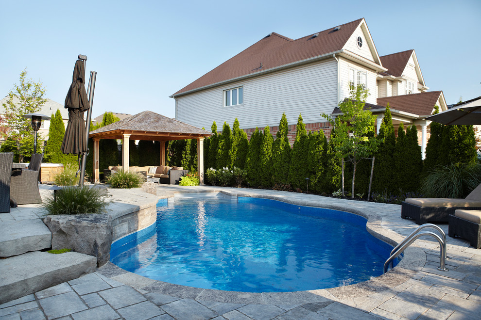 Diseño de piscina con fuente natural actual grande a medida en patio trasero con adoquines de piedra natural